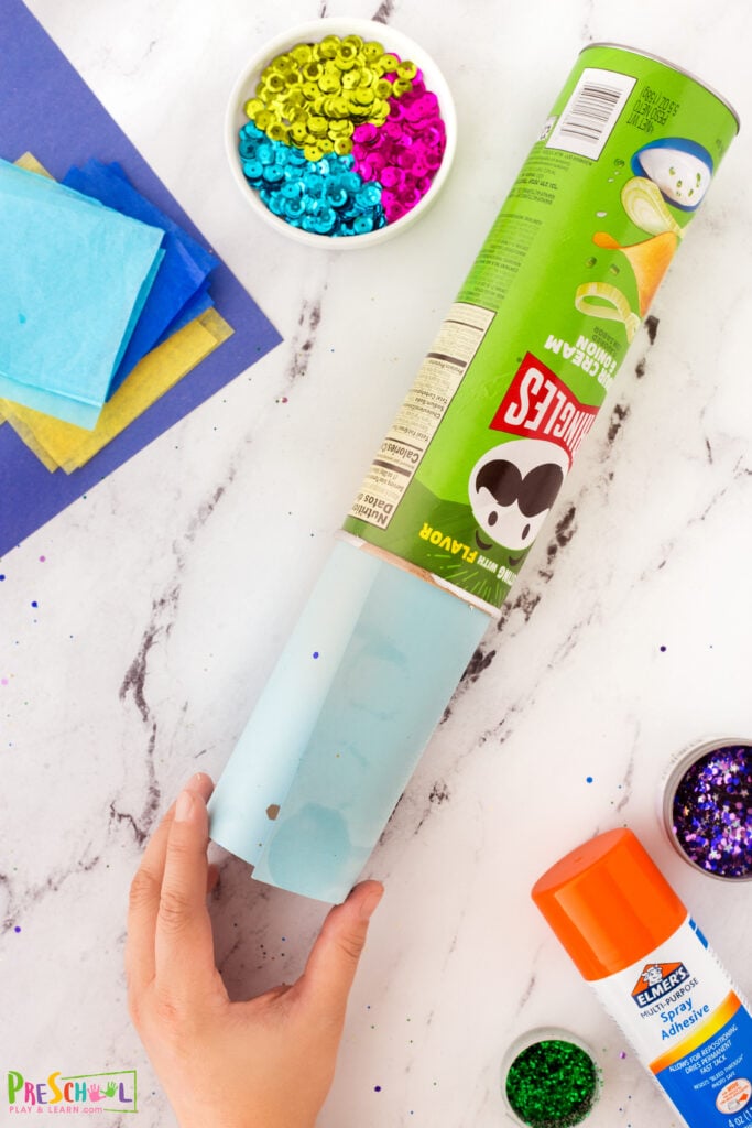 Once  the glitter is securely in place and the glue has dried, roll the paper with the glitter side inwards and slide it into an empty, wiped clean Pringles can. Tack the paper down with glue if necessary and cut off any excess that is sticking from the can. 